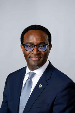 President Ben Vinson, III wearing a blue suit, white shirt, light blue tie and black glasses.